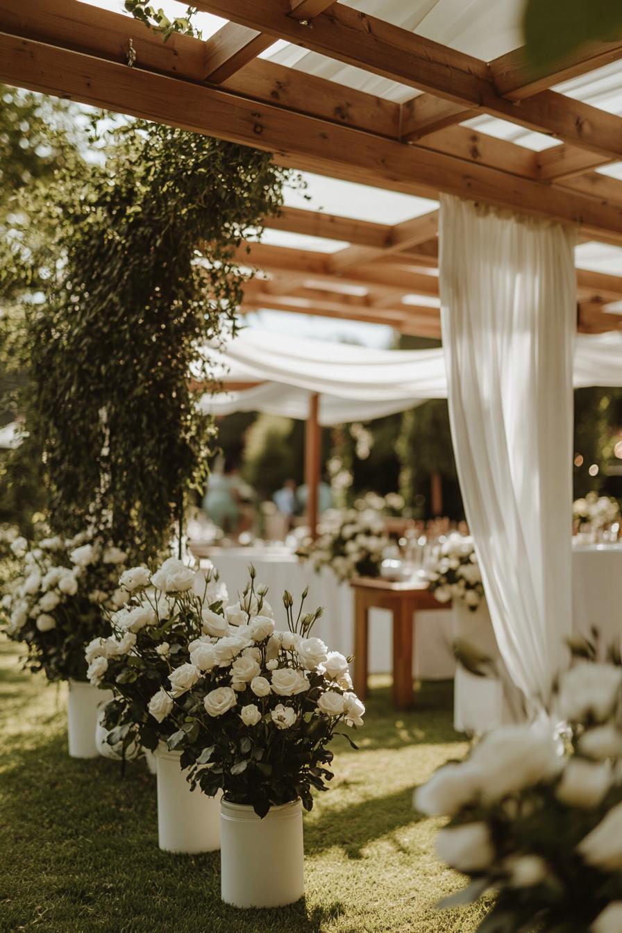 White roses and greenery under wooden pergola with flowing draped fabric